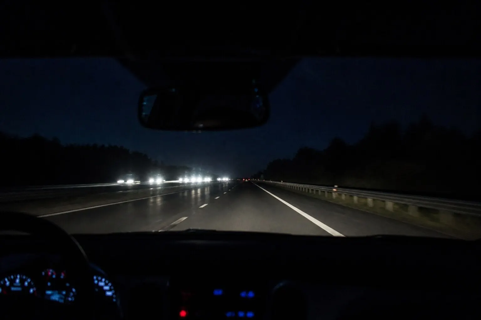 Gece otoyolunda araç içinden ön cama bakış, gösterge ışıkları ve karşıdan gelen farlar